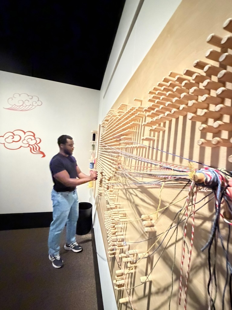 me putting a thread on the world map string art board showing migration to bc